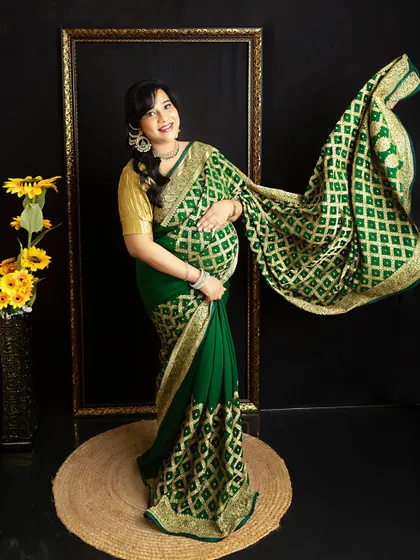 A stunning portrait in a green bandhani saree. The fabric is tossed to showcase its beautiful pattern and flow against a dark, modern backdrop.