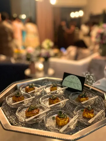 A server holding a tray of our signature appetizers at a festive house party. The blurred background shows a lively party, highlighting how our seamless service allows hosts to relax and enjoy their own event.