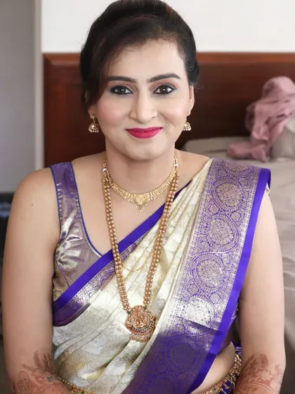 A sophisticated look for Manisha attending her brother's Muhurtham. The makeup is clean and classic, with a defined eye and a bright red lip that contrasts beautifully with her off-white and purple Kanchipuram saree.