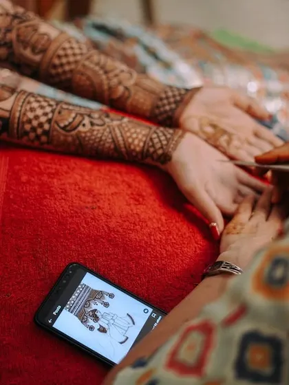 A behind-the-scenes look at the mehndi artist at work, using a phone for the design reference. It shows the modern reality of this traditional art form.