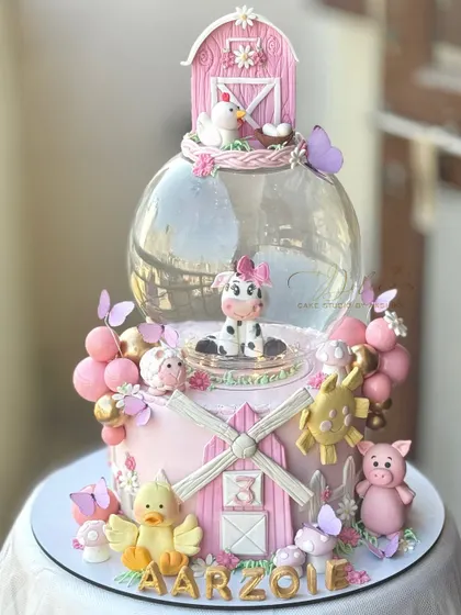 A pink farmland theme cake for a third birthday. This design features a globe tier and lots of cute, hand-modelled farm animals like a cow, pig, and chicken.
