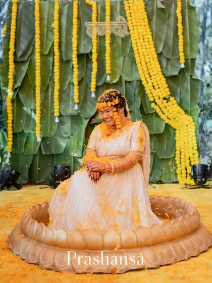 A beautiful portrait of the bride seated in a large vessel for her Haldi ceremony, smiling contentedly.