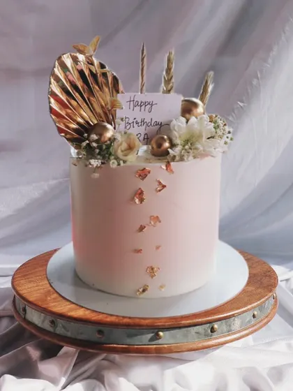 A lovely pastel pink cake with gold leaf accents, topped with dried golden palm spears and delicate white flowers for a boho-glam look.