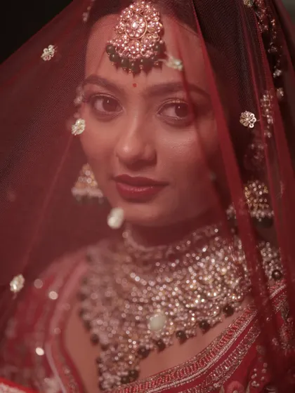 A captivating shot of my bride Krupa through her red veil. Her look features soft, sculpted skin, a flush of rose, and bold eyes for a timeless bridal glow.