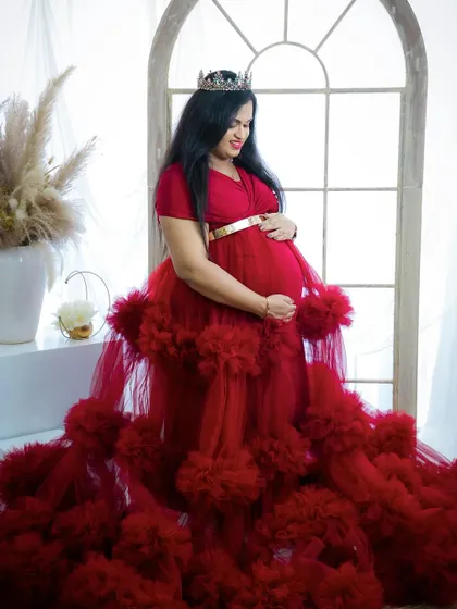 A regal and radiant portrait. The mom-to-be wears a tiara and a stunning red gown, her expression full of joy and anticipation.