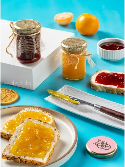 Jars of homemade fruit jam, styled with fresh bread and a vibrant blue background for a fun, product-focused shot.