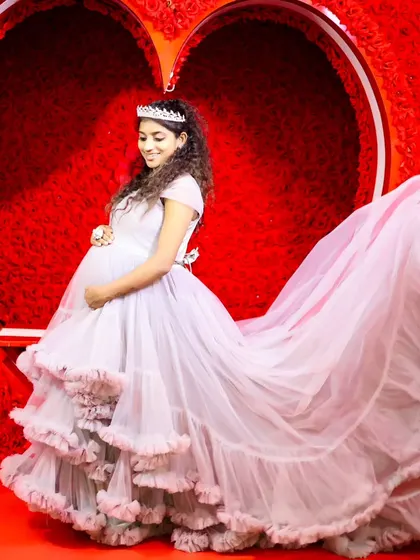 A beautiful maternity shot with the long trail of a light purple gown spread out, creating a dramatic effect against the red heart backdrop.