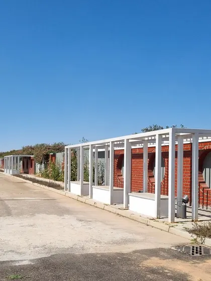 A view of the entrance walkway at Aamby City, featuring pergolas with built-in seating. This structure provides shade and defines the pedestrian path, creating a rhythmic and inviting journey into the township.