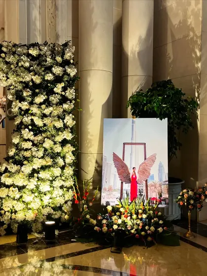 A personalized corner at an event at The Leela Palace. A large portrait of the bride is displayed on an easel, surrounded by beautiful floral arrangements and a towering structure of white flowers.