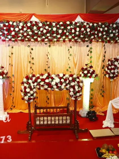 A beautiful naming ceremony decoration in classic red and white. The setup includes a traditional wooden cradle decorated with a floral arch, and a personalized photo frame of the baby.