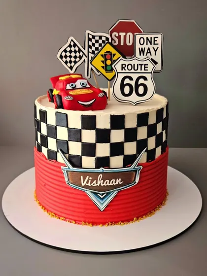 The Lightning McQueen! A vanilla cake for Vishaan, designed with the iconic red race car from the movie 'Cars', complete with a checkered flag pattern.
