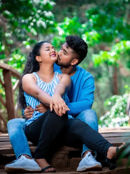 A fun and intimate pre-wedding photo capturing a sweet kiss on the cheek in a natural, rustic setting.
