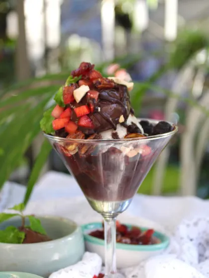 A full view of the chocolate sundae in its glass, highlighting the generous toppings of berries and nuts.