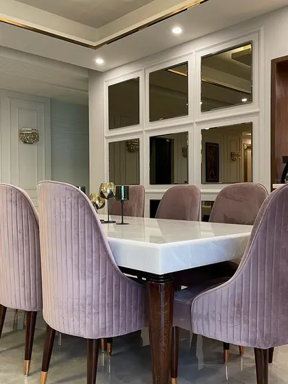 A view of the dining setup, featuring plush, channel-tufted chairs in a dusty rose velvet. The design is complemented by a mirrored accent wall that adds depth and reflects the soft lighting of the space.
