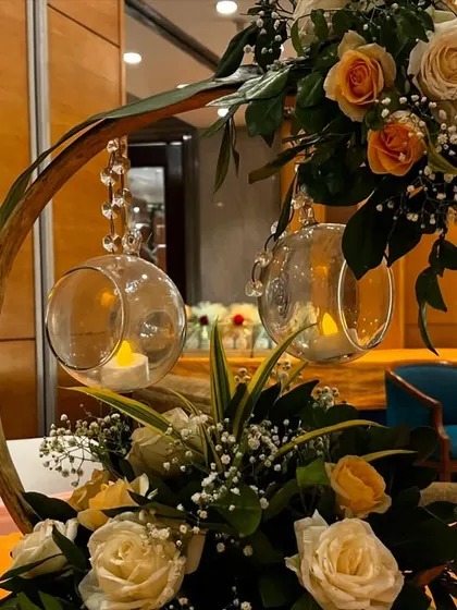 A rustic yet elegant centerpiece from an event at Jaypee Siddharth. The design uses a wooden ring, hanging candle orbs, and a beautiful arrangement of peach and white roses.