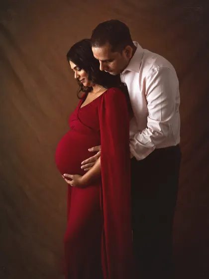 A quiet and intimate portrait of an expecting couple. The husband stands behind his wife, both gently holding her belly, creating a sense of protection and shared anticipation.