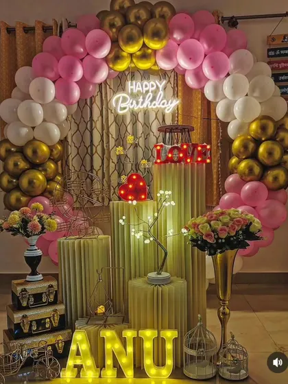 An elegant and romantic birthday decoration perfect for a surprise at home. The pink, white, and gold balloon arch, combined with light-up letters and props, creates a warm and celebratory feel.