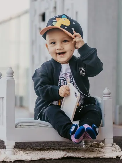 A close-up shot of a happy baby boy in a cap, enjoying his modern poolside photoshoot on a tiny white bed.