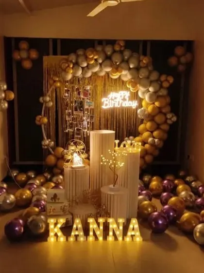 A warm and inviting birthday setup for Kanna. A gold, silver, and purple balloon arch is combined with a photo display, neon sign, and illuminated letters for a personalized touch.