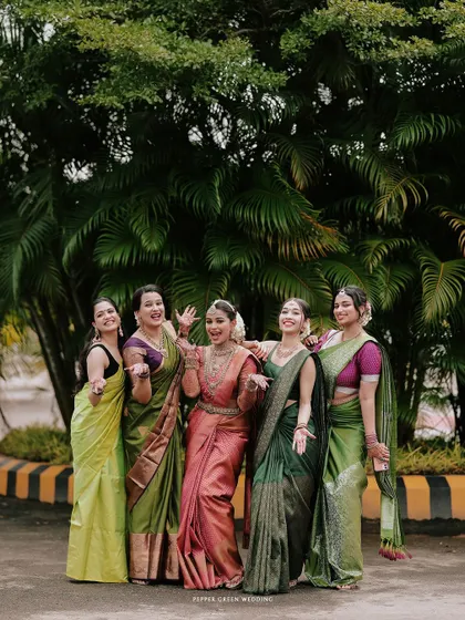 The bride, Arya, and her bridesmaids sharing a fun, candid moment. The vibrant green sarees create a beautiful color palette against the natural background.