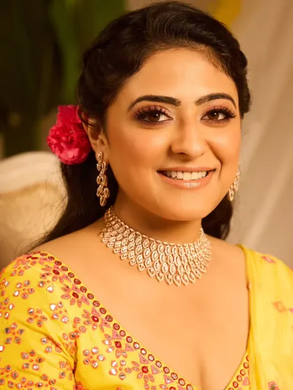 A close-up of the model's face for this Haldi look. The makeup is fresh and glowing, and a single pink flower adds a pop of color.