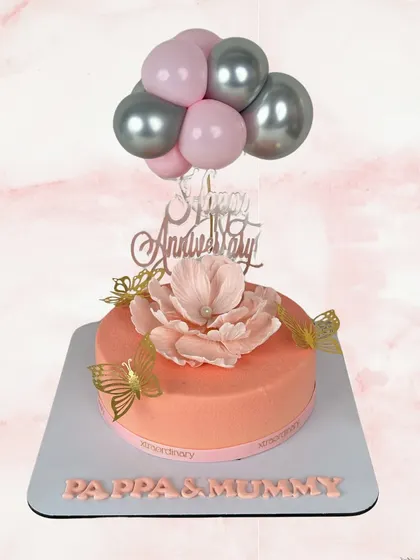 A fun and whimsical anniversary cake for "Pappa & Mummy". The design features a cascade of pink and silver balloons, a beautiful sugar flower, and delicate golden butterflies.