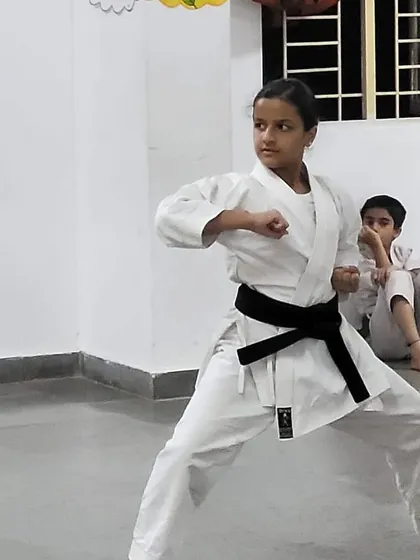 A young black belt student demonstrates a sharp technique during her belt exam, holding a strong stance that shows focus and control.