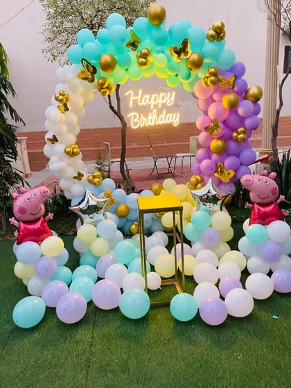 A Peppa Pig themed outdoor party with a rainbow balloon arch and character cutouts.