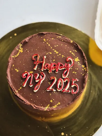 A mini chocolate cake with "Happy NY 2025" piped on top, perfect for a small celebration.