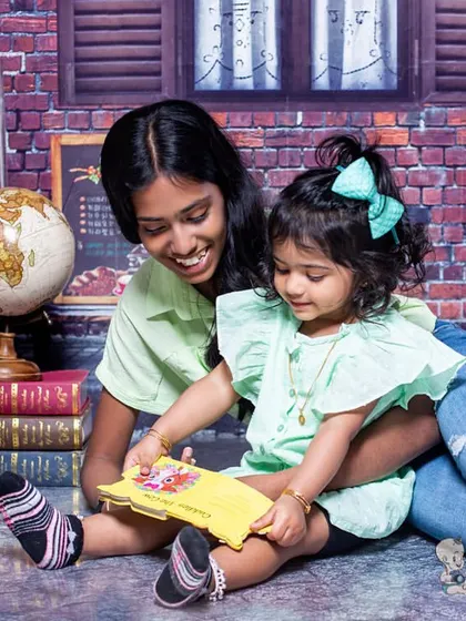 An older sister reads a book to her younger sibling in a cozy, street-cafe themed setting. This is a sweet moment that captures the joy of sharing stories together.