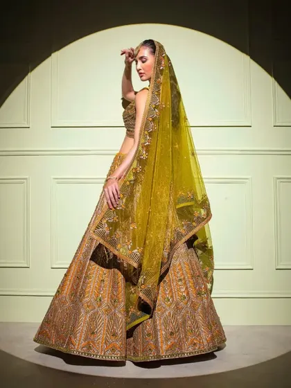 A side profile of the regal gold bridal lehenga, showcasing the volume of the skirt and the intricate detailing on the dupatta.