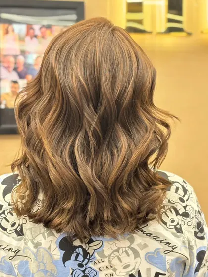 The back of a client's hair, showing a beautiful color blend styled into soft waves. The look is fresh, modern, and full of dimension.