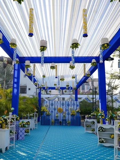 A stunning 'Blue Mirage' themed Haldi ceremony. The entire walkway is decorated in shades of blue and white, with a patterned blue carpet and hanging floral elements.