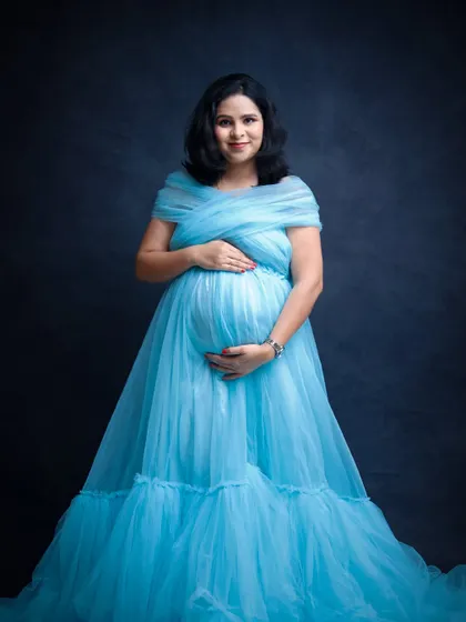 A classic maternity portrait in a beautiful blue gown against a dark, textured backdrop. The simple, elegant pose highlights the joy of the mother-to-be.