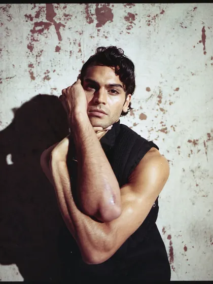 An archival shot from a menswear editorial, captured on Kodak Portra film. The image has a raw, textured quality, with dramatic lighting highlighting the model's pose and expression.