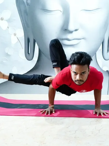A student holds a challenging arm balance, Eka Pada Koundinyasana, with intense focus.
