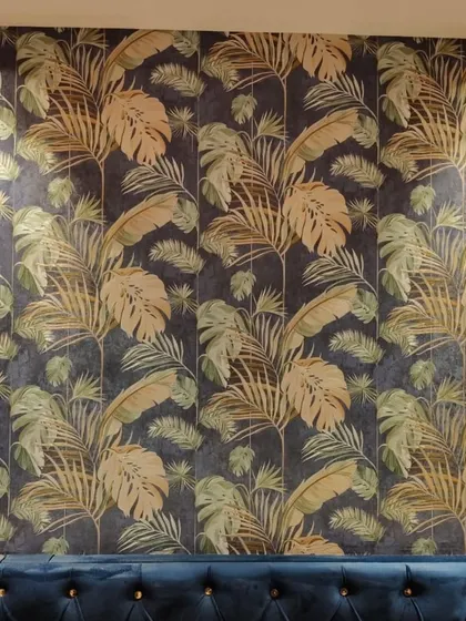 A sophisticated tropical leaf wallpaper in dark blue and gold. This design is perfect for a lounge or dining area, creating a luxurious and moody ambiance.