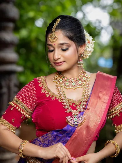 A candid shot of a bride in a red and purple silk saree, showing her natural joy. This outfit is perfect for capturing the happy moments of your special day.