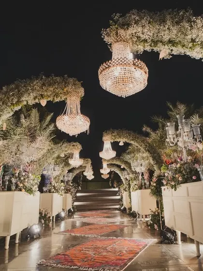 An enchanting entryway with arches made of baby's breath and foliage, with crystal chandeliers hanging at intervals, leading guests down a path of Persian rugs.