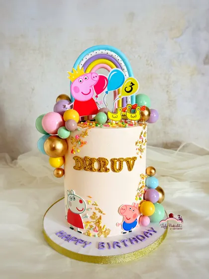 A tall and festive Peppa Pig cake, decorated with a balloon bouquet, a rainbow, and the whole family. The gold confetti adds a touch of sparkle.