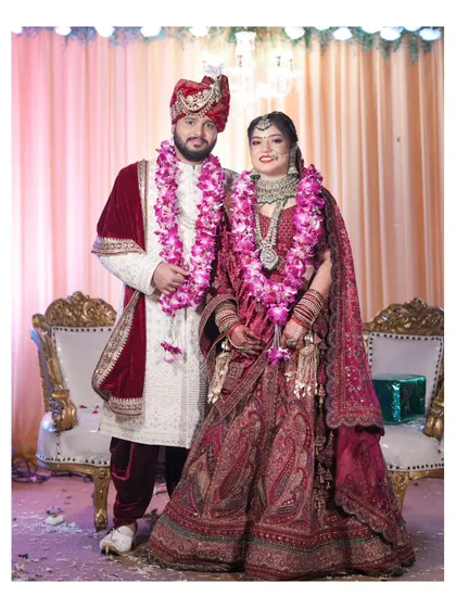 A classic formal portrait of the bride and groom on their wedding day, seated on elegant chairs.