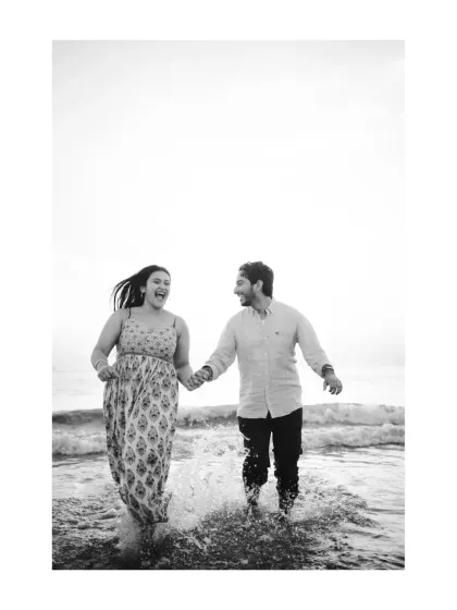 A playful moment in black and white, as the couple runs through the shallow water. The motion and splashes create a dynamic and joyful image that feels full of life.