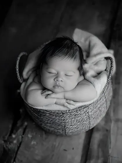 A simple basket pose in black and white creates a timeless and artistic feel. The focus remains entirely on the baby's serene expression and tiny, folded arms.