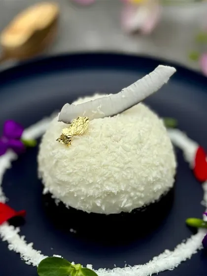 A dome of pure white coconut mousse, topped with a sliver of fresh coconut and a touch of gold leaf. This dessert is a tribute to tropical flavours, presented with elegance and simplicity.