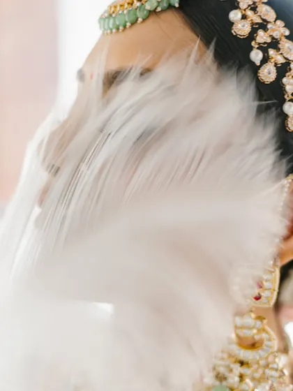 An artistic close-up, with a white feather gently brushing the bride's face, creating a soft, dreamy, and high-fashion look.