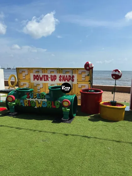 A 'Power-Up Snaps' photo booth for a Super Mario party, complete with a warp pipe for kids to play in and piranha plant props, all set against a beautiful beach view.