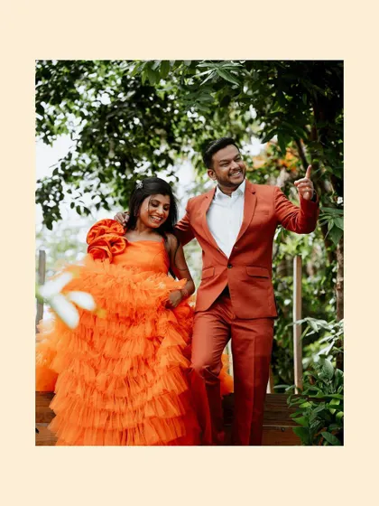 A vibrant, happy shot of the couple in bright orange outfits, walking down a staircase surrounded by lush greenery.