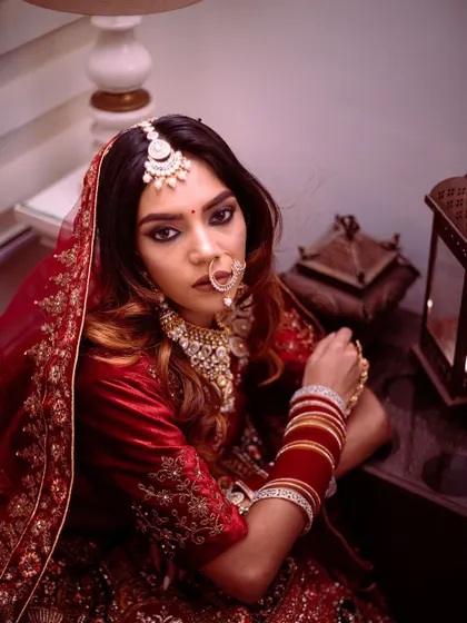 For me, a bridal portrait is about capturing a feeling. Here, I used moody, dramatic lighting to highlight the bride's intense gaze and the rich velvet of her traditional red lehenga, creating a look that is both fierce and timeless.