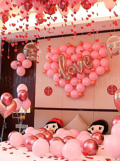 A sweet and charming room decoration featuring a large heart made of pink balloons with a "Love" sign. This setup is perfect for anniversaries or Valentine's Day, with cute character pillows adding a playful touch.