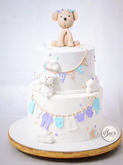 A lovely two-tier baby shower cake with a clothesline of baby clothes, fluffy clouds, and a cute puppy topper.
